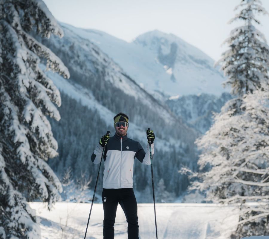 Langläufer auf einer gespurten Loipe zwischen schneebedeckten Bäumen und Bergen in Tirol.