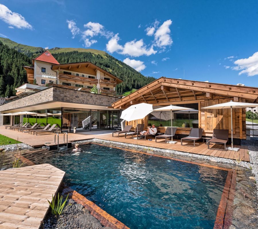 Das Alpinhotel Berghaus im Zillertal mit Naturschwimmteich und Liegen.