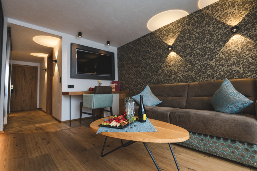 Gemütlicher Wohnbereich mit Fernseher, Sofa und Holzeinrichtung im Alpinhotel Berghaus in Tux.