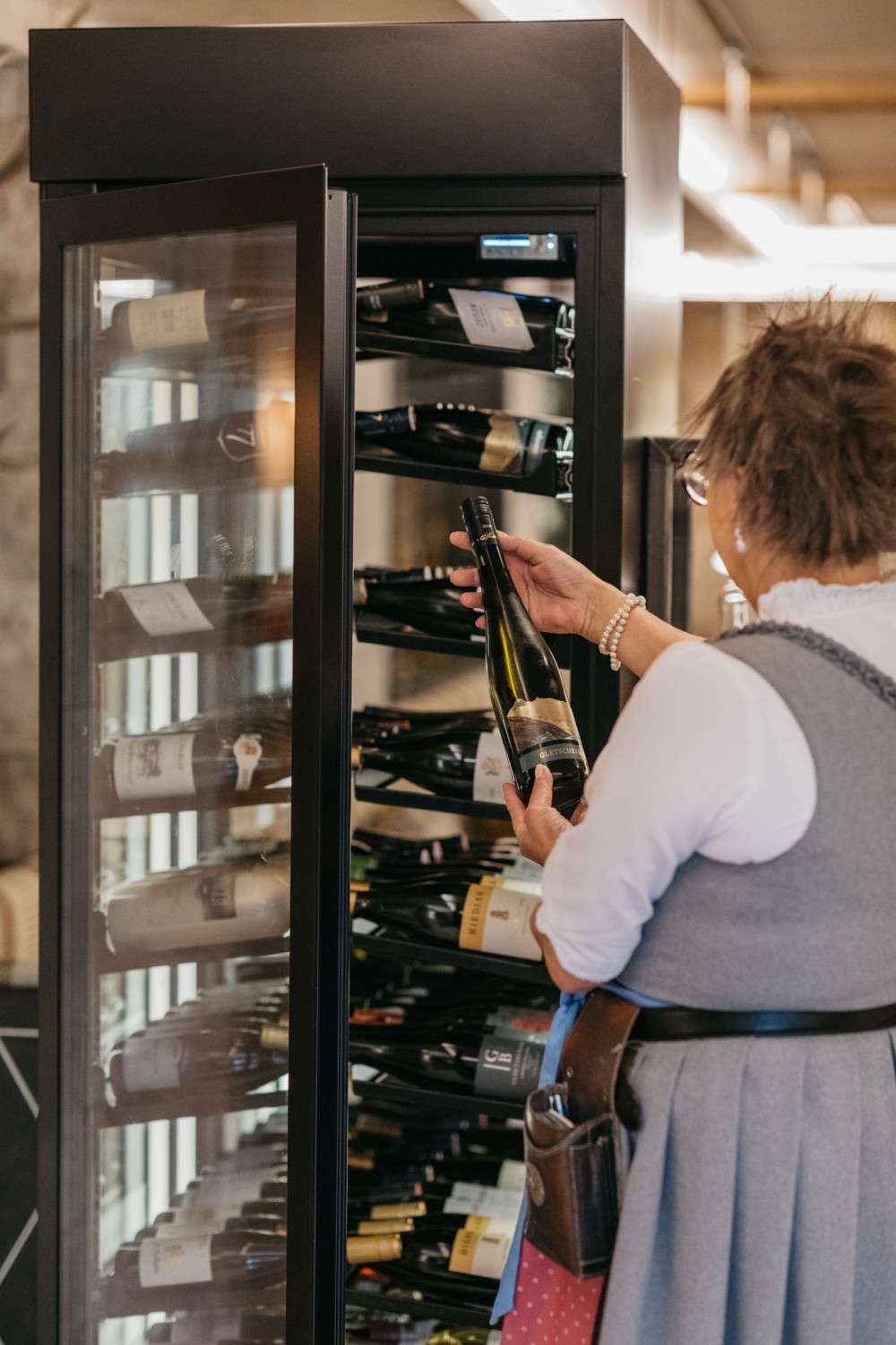 Servicemitarbeiter schenkt einer Frau am gedeckten Restauranttisch Wein ein im Alpinhotel Berghaus in Tux.