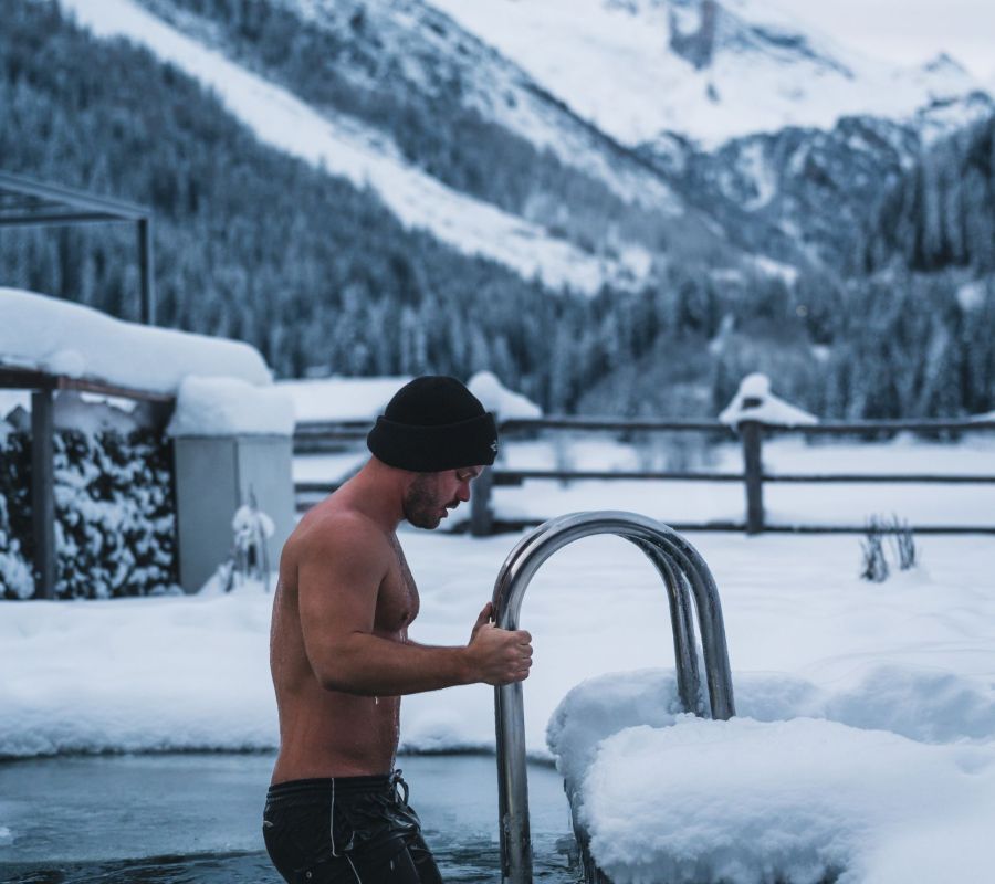 Mann steigt aus einem Außenbecken inmitten einer verschneiten Berglandschaft beim Alpinhotel Berghaus in Tux.