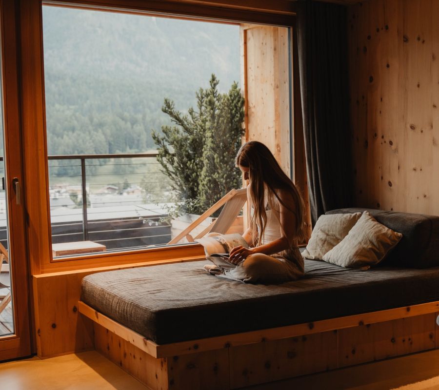 Junge Frau lesend auf ihrem Hotelbett beim Wanderurlaub für Alleinreisende in Südtirol.