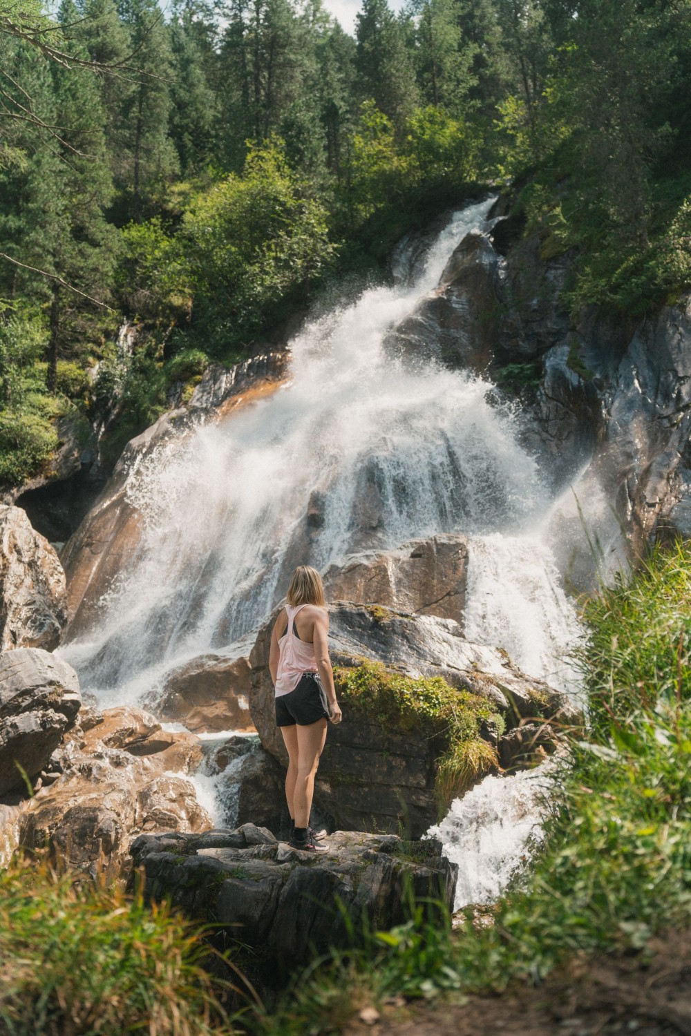 Wanderer machen eine Pause an einem Wasserfall zwischen Felsen und grünen Berghängen im Zillertal.