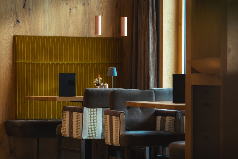 Hotelbar mit gepolsterten Barhockern, Holzverkleidung und gedämpftem Licht im Alpinhotel Berghaus im Zillertal.