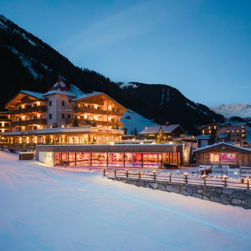 Das Alpinhotel Berghaus in Tux liegt tief verschneit und beleuchtet in der winterlichen Abenddämmerung.