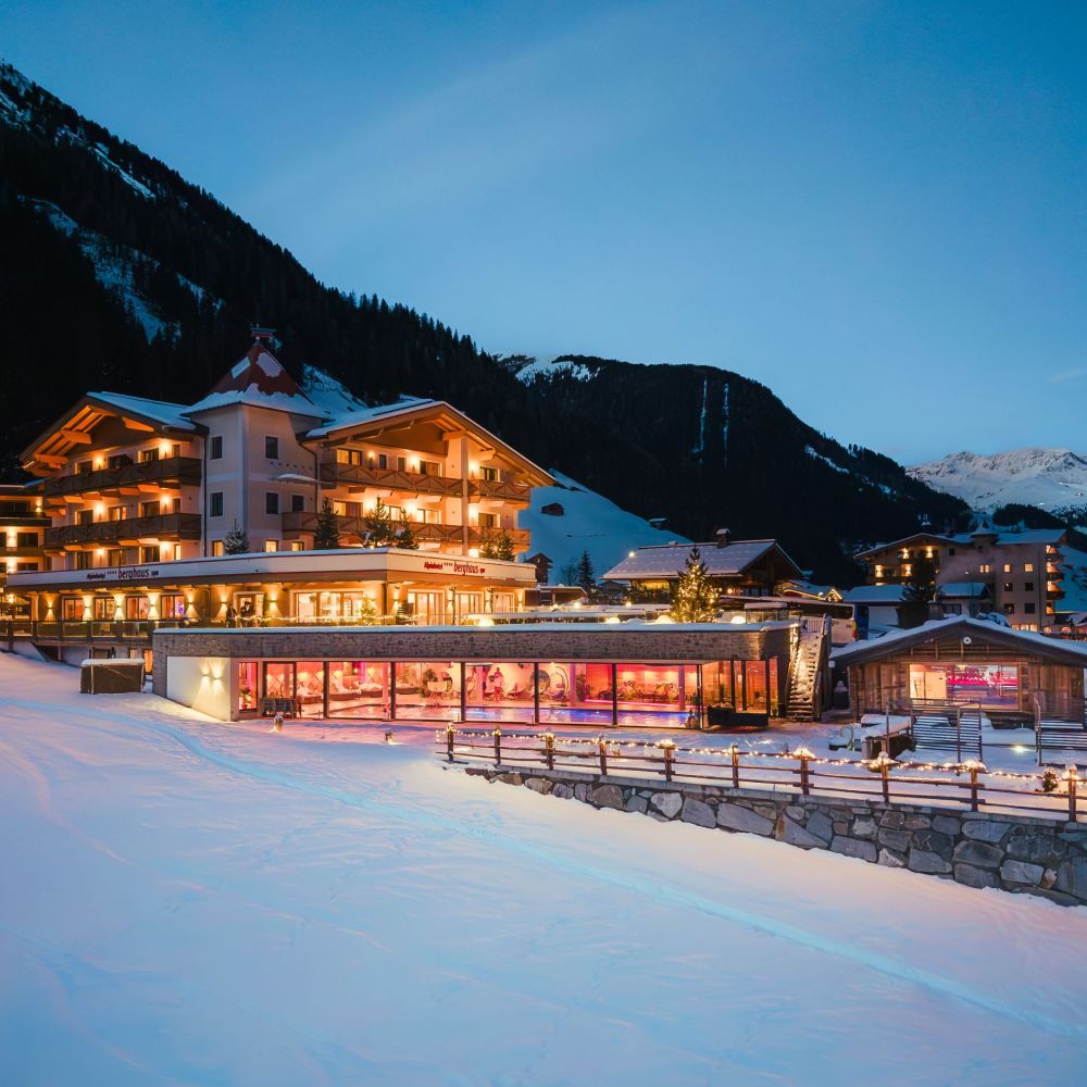 Das Alpinhotel Berghaus in Tux liegt tief verschneit und beleuchtet in der winterlichen Abenddämmerung.
