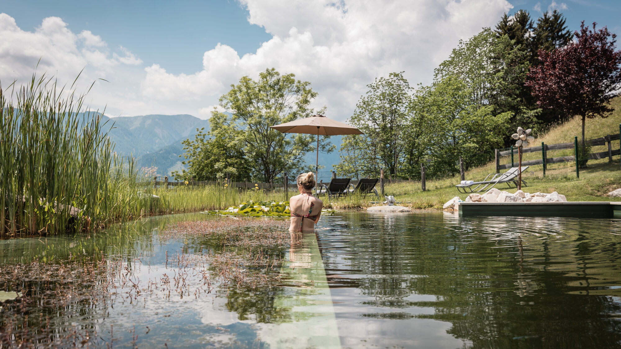 A young woman swims in a beautiful natural swimming pond in the breathtaking mountains of Carinthia, Austria