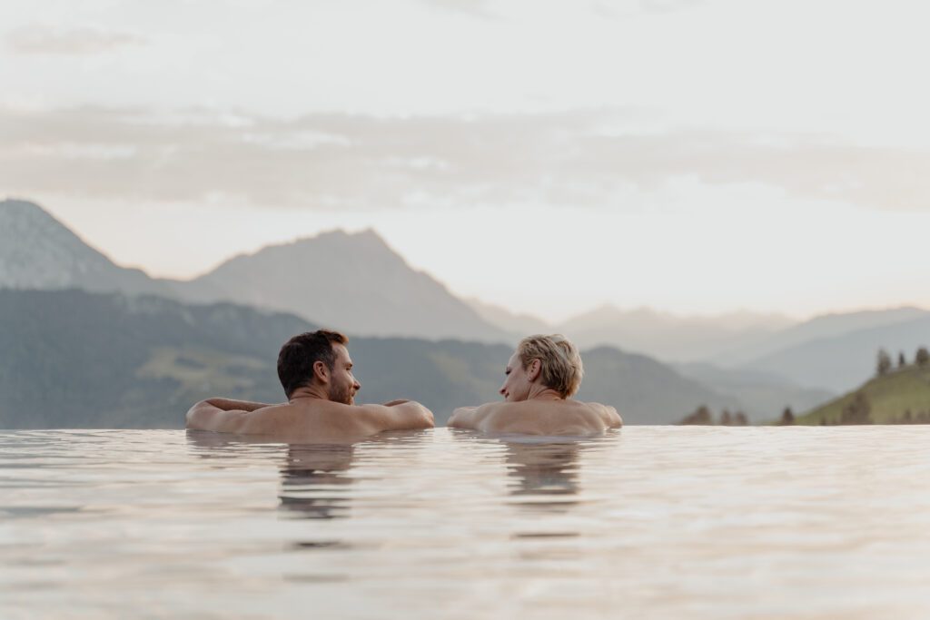 Pärchen am Rand von einem Infinitypool mit Blick in die Berge