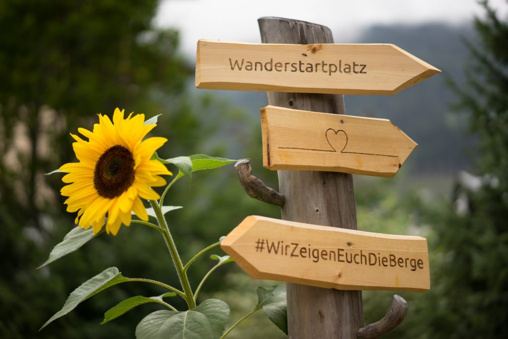 Wanderstartplatz vom Wanderhotel Alte Post in Großarl. Wegweiser aus Holz neben einer Sonnenblume.