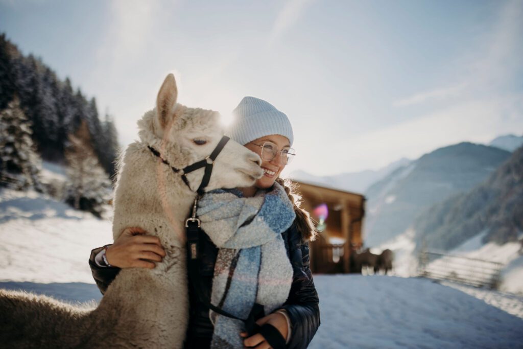 Frau umarmt Alpaka vor winterlicher Landschaft