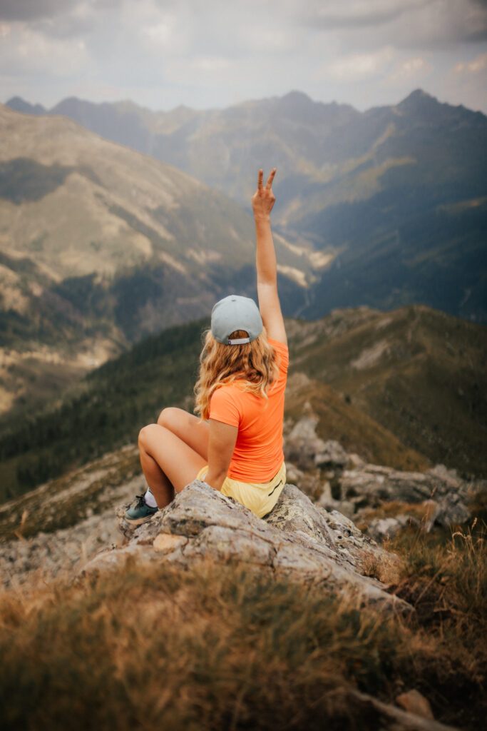 Frau beim Wandern sitzt auf einem Stein und blickt ins Tal