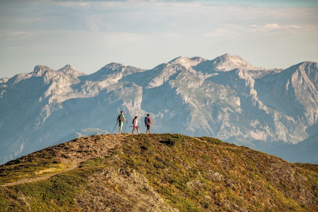 Drei Menschen auf einer Graskuppe vor Bergpanorama