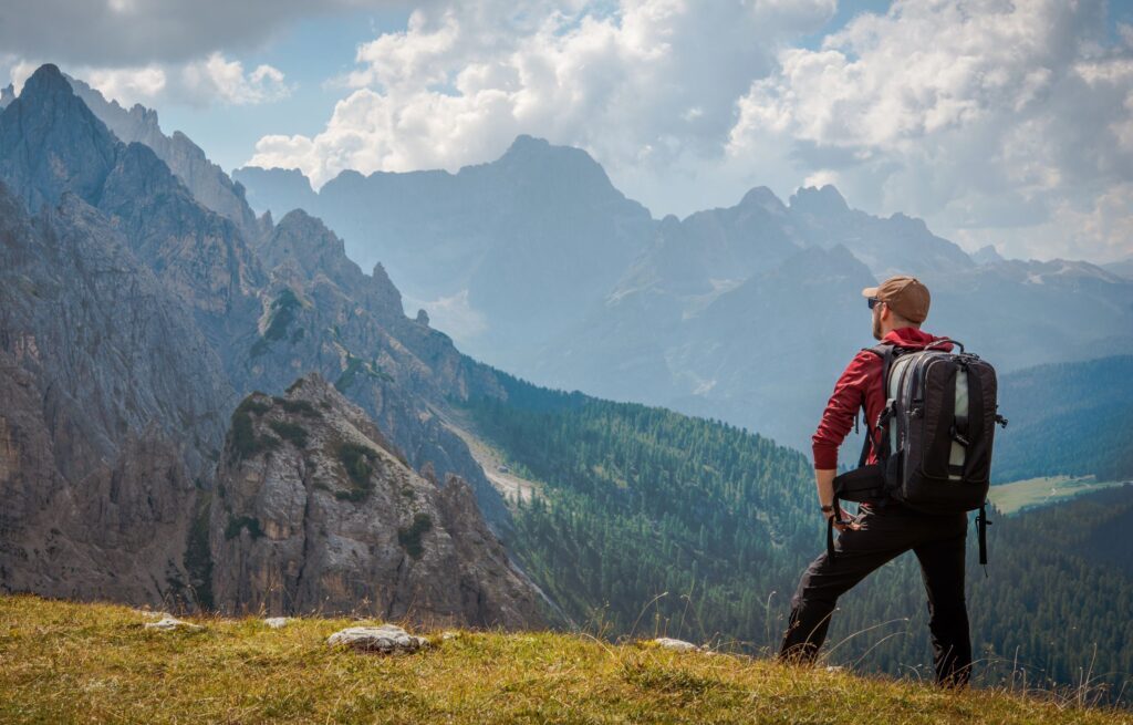 Mann steht auf Almwiese und genießt Ausblick