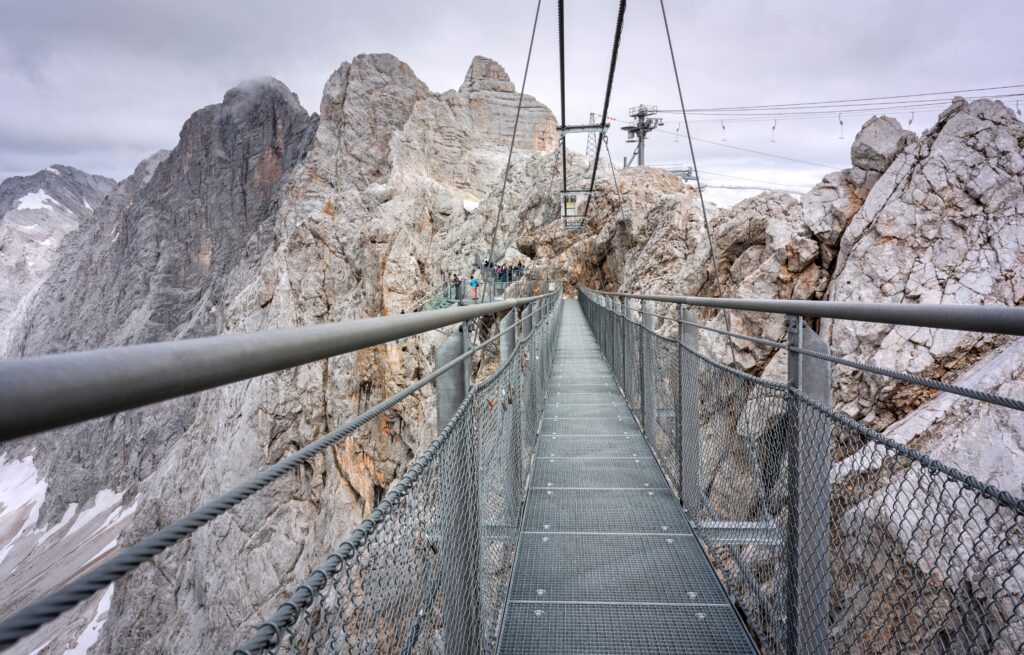 Die Dachstein Hängebrücke führt schmal über die Tiefe auf eine graue Felswand des Dachsteinmassivs hin.