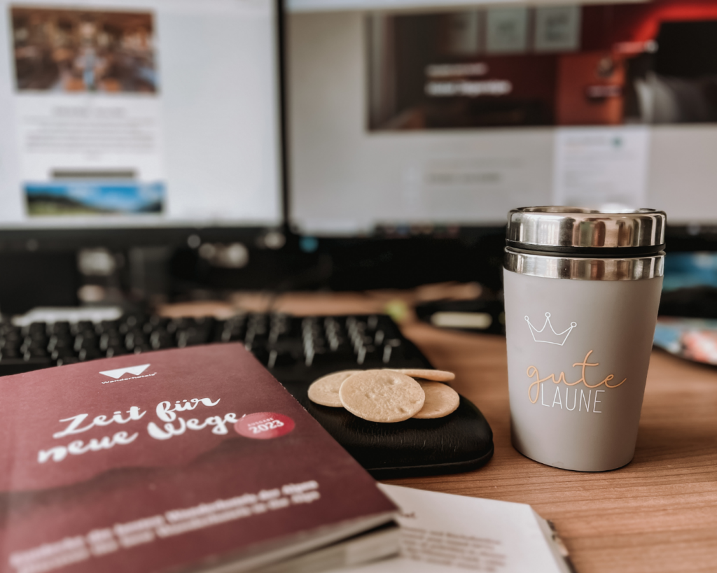 Ein Arbeitsplatz bei den Wanderhotels mit Kaffee und Keksen und dem Hotelkatalog