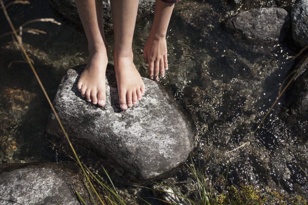 Nackte Füße auf einem grauen Stein, der in kristallklarem Wasser liegt