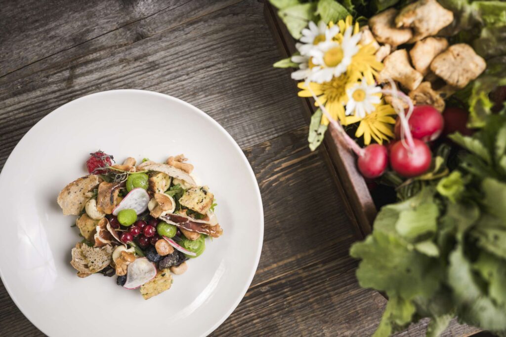 weißer Teller auf Holztisch mit hübsch angerichtetem Salat und Radieschen und Blumen als Deko