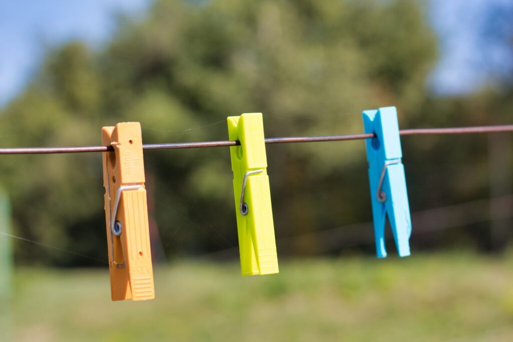 Drei Wäscheklammern hängen an einer Wäscheleine mit Natur im Hintergrund