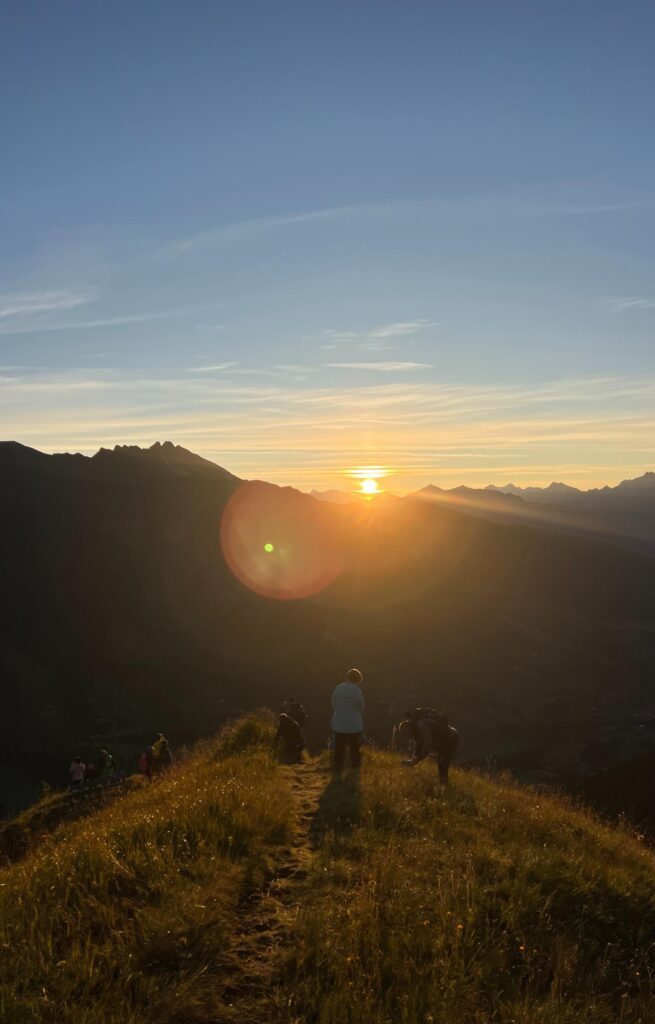 Sonnenaufgang auf der Stollespitze in Südtirol. Wanderer vom Erlebnisort Gassenhof stehen am Gipfel.