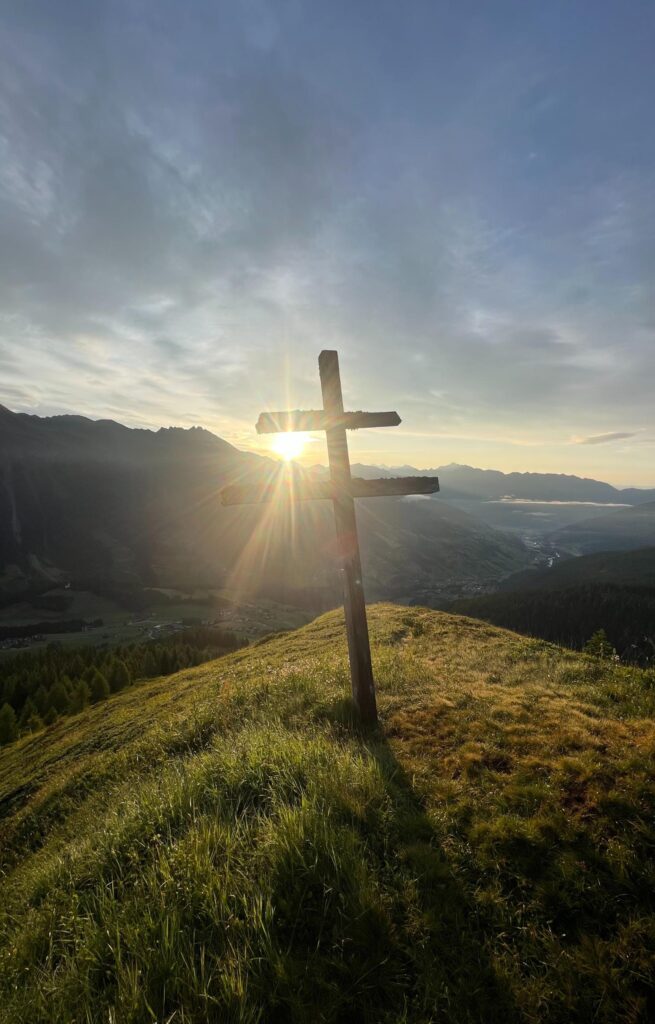 Sonnenaufgang auf der Stollespitze in Südtirol. Gipfelkreuz aus Holz in der Morgensonne.