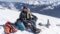 Pärchen sitzt auf dem Rodel und mach Pause Winterliche Landschaft im Hintergrund(c)Wildkogel-Arena