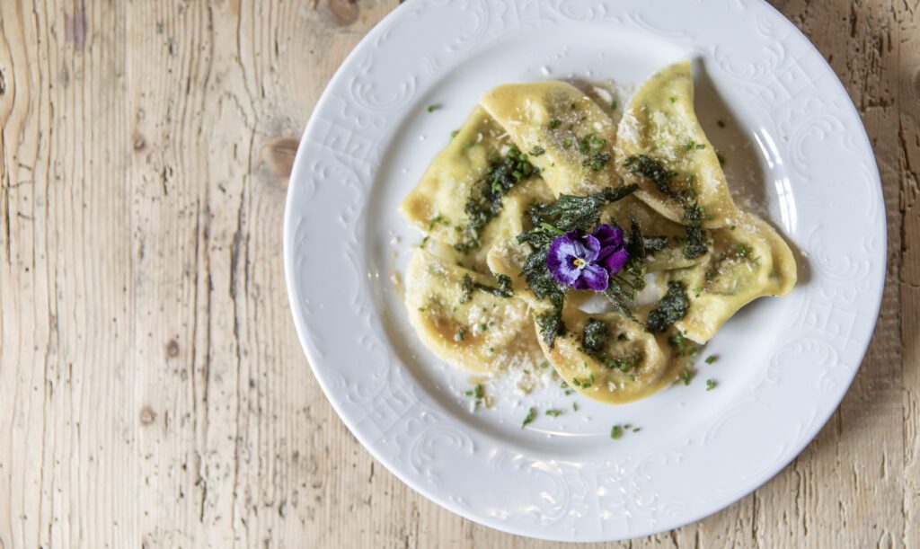 Südtiroler Schlutzkrapfen, hübsch angerichtet mit Kräutern und essbarer Blüte