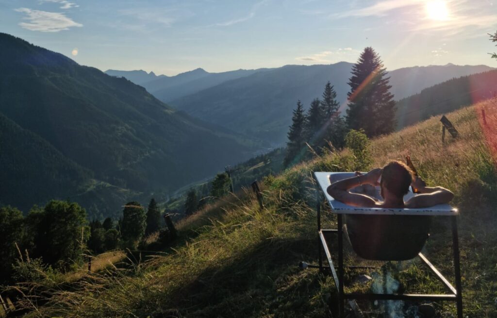Mann sitzt in einer Badewanne im Freien mit Blick über das Tal von Vorderglemm
