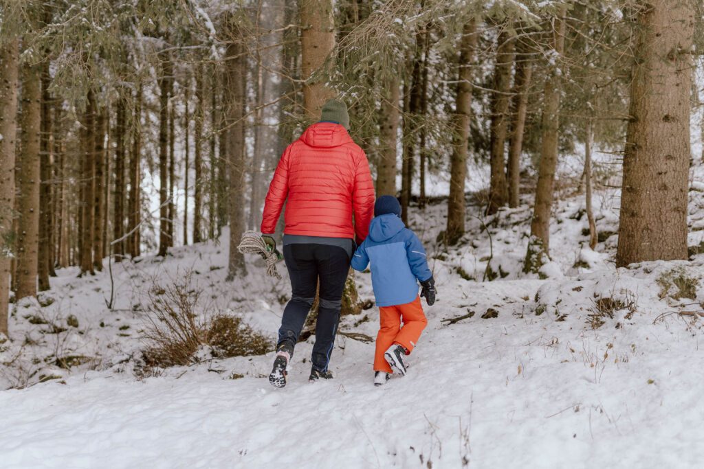 Weihnachtstradition im Antholzer Tal: Ein Vater und sein Kind holen gemeinsam einen Tannenbaum aus dem verschneiten Wald für das Wanderhotel Vierbrunnenhof