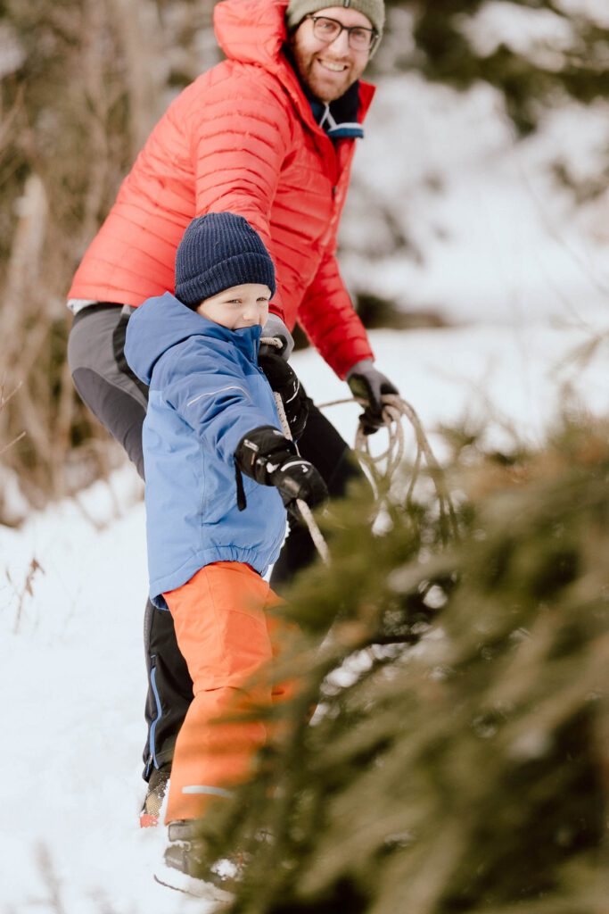 Weihnachtstradition im Antholzer Tal: Ein Vater und sein Kind holen gemeinsam einen Tannenbaum aus dem verschneiten Wald für das Wanderhotel Vierbrunnenhof