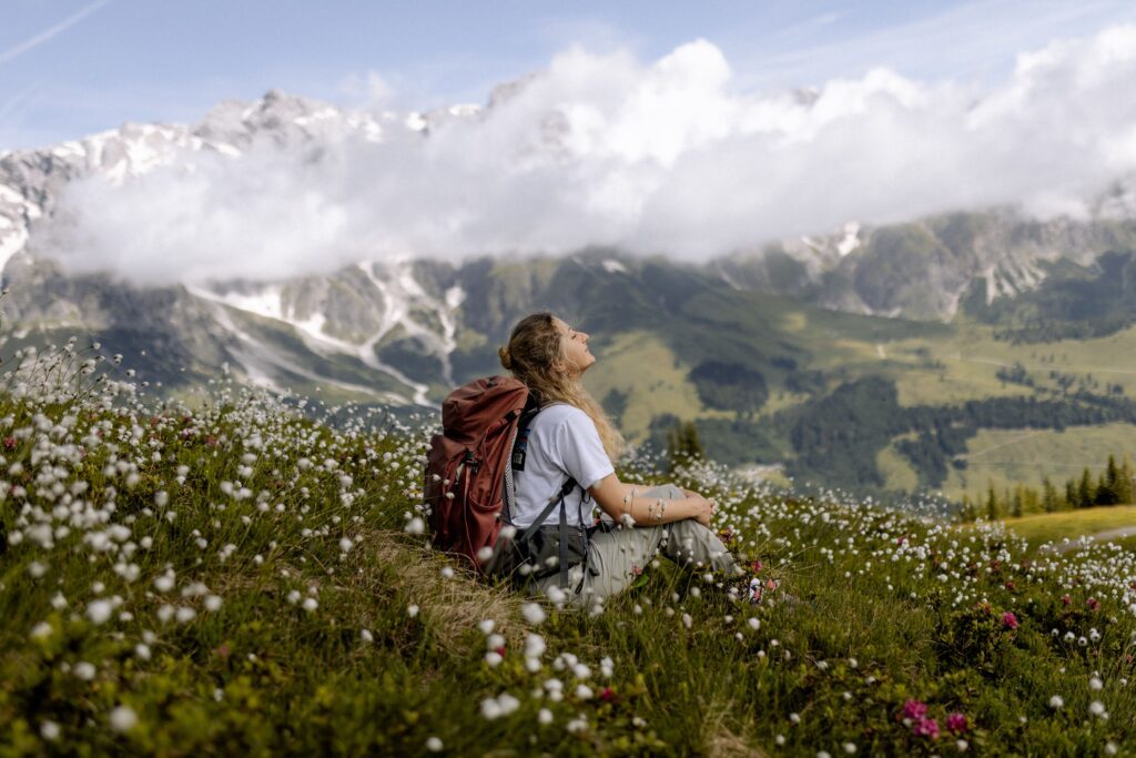 Frau sitzt in einer Blumenwiese im Frühling bei einer Wanderung am Hochkönig