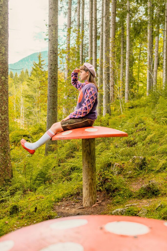 Frau sitzt auf überdimensionalem Fliegenpilz beim Wanderurlaub im Wanderhotel Glemmtalerhof im Salzburger Land